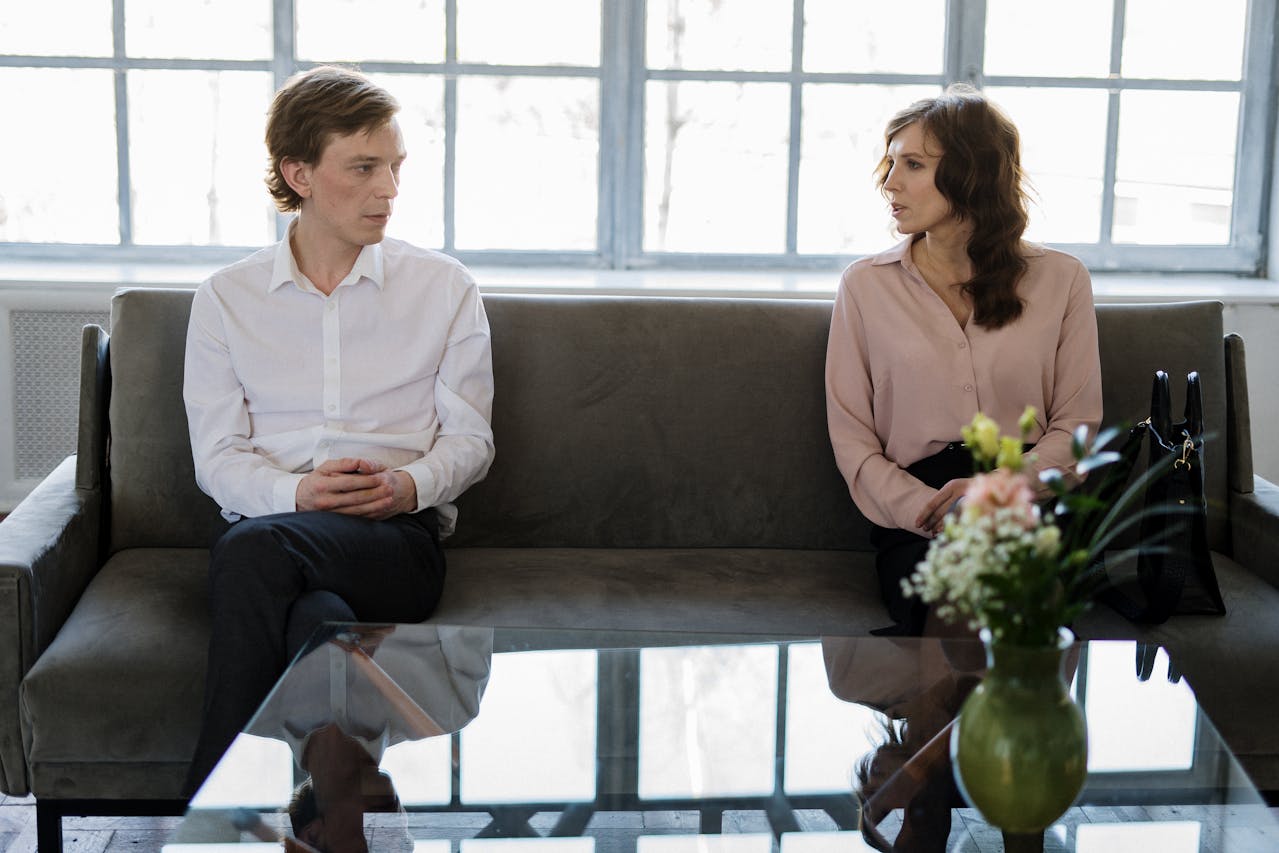 A man and a woman sit apart on a sofa, appearing to have a tense conversation.