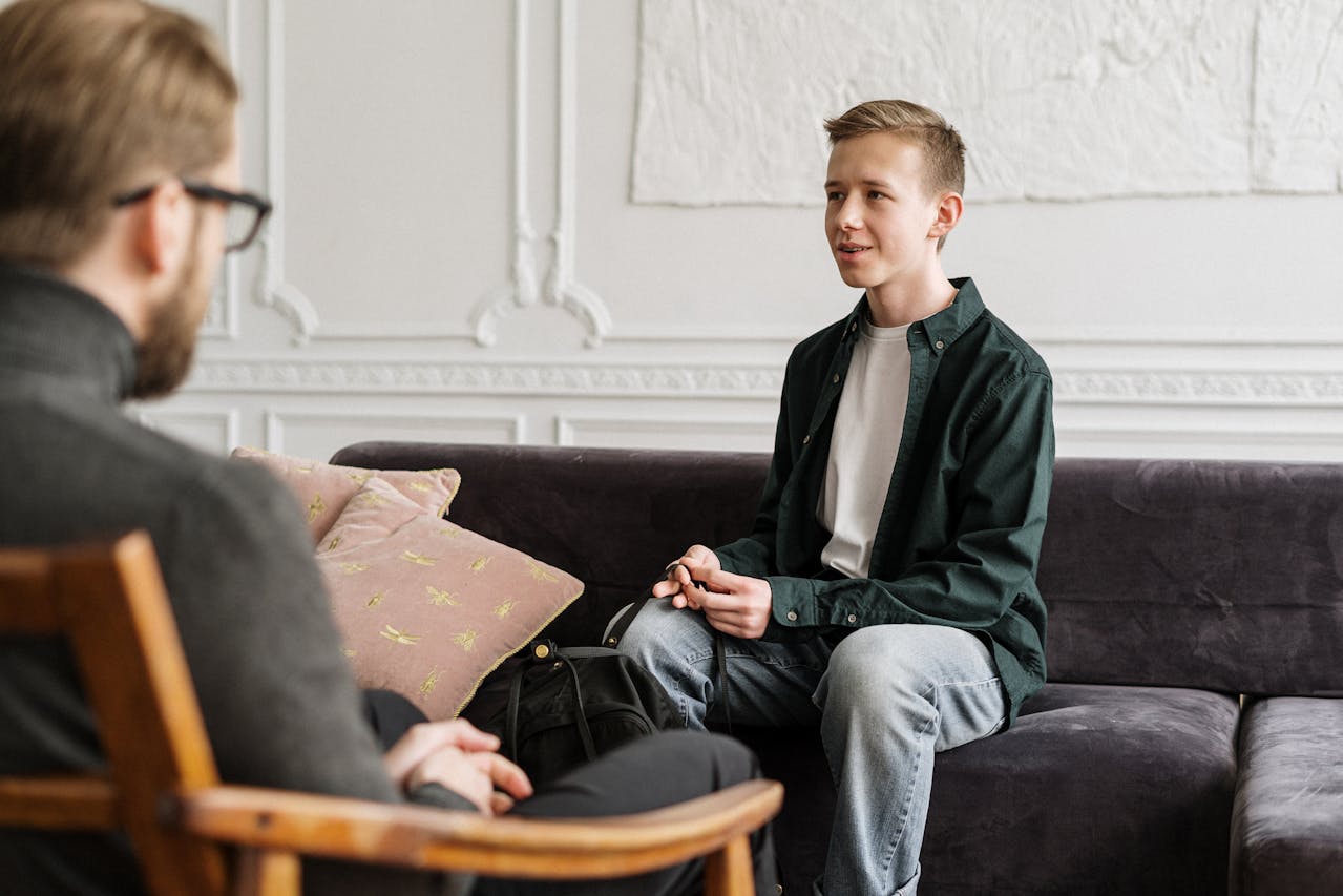 A teenage boy talks with an adult during a casual therapy session in a cozy room.